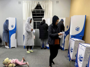 A young girl playing with her teddy bear while people are voting 