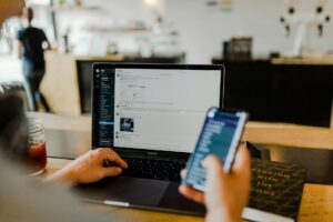 A person working on the laptop while holding a phone