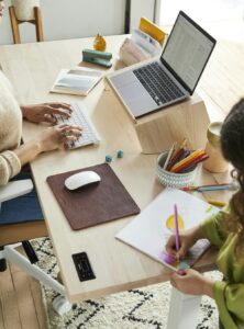 A woman sitting at a table with a child while using laptop